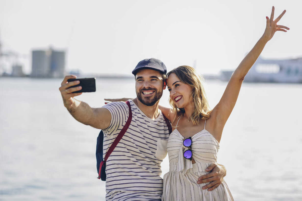 Spain, Andalusia, Malaga, happy tourist couple taking selfie with smartphone at the coast